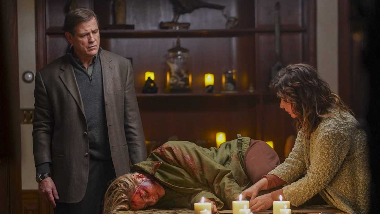A bloodied woman laying on a table next to nine lit candles in 'The Puppetman'