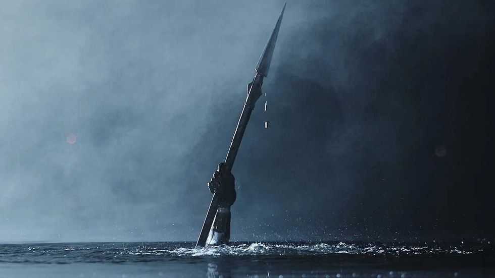 A hand holding a spear emerging from a lake in Teenage Sex and Death at Camp Miasma