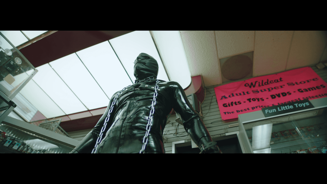 A man in a black gimp outfit at a sex store in 'Hometown Boys'