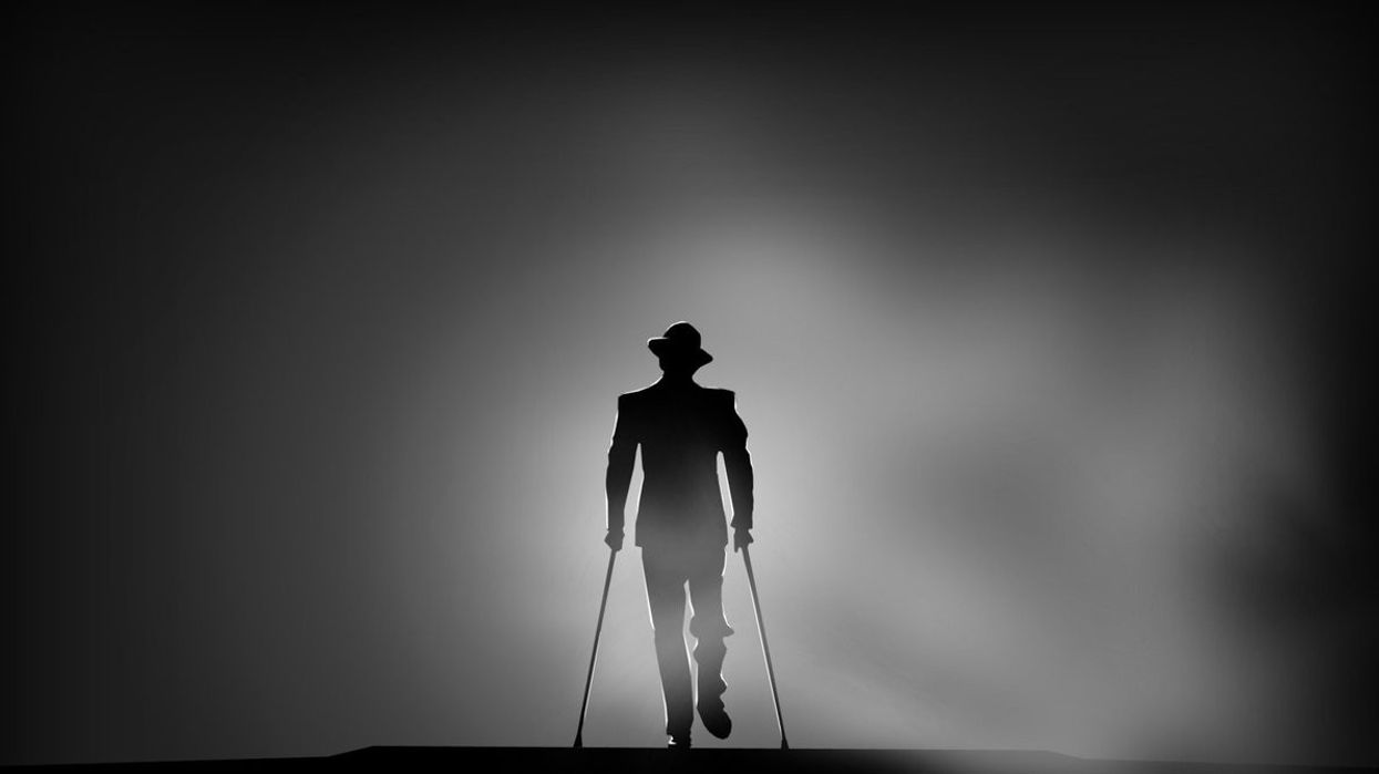 A man in a suite on crutches walks up while being backlit
