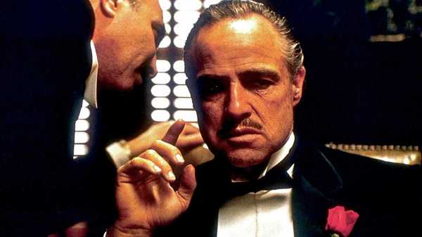 A man whispering into the ear of Marlon Brando as Don Corleone in The Godfather