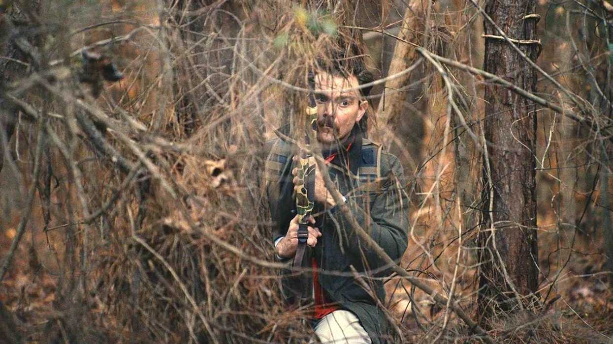 A man with a rifle hidding in the woods.