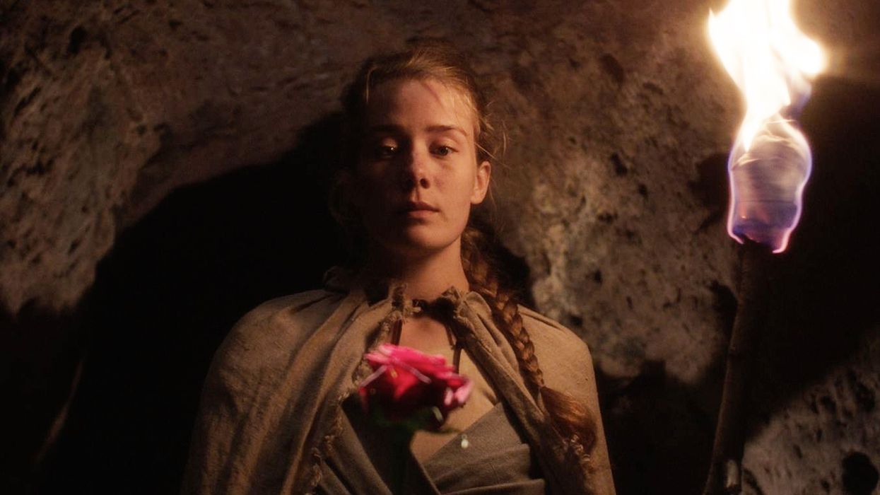 A woman holds a flower and a torch in a cave in 'Belle'