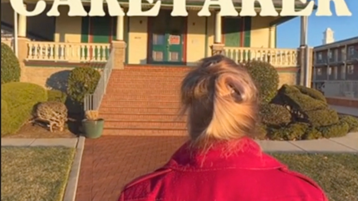 A woman in a red jacket walking into a Victorian style house in 'Caretaker'