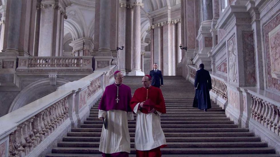 Alt Text: John Lithgow and Ralph Fiennes walk down the stairs at the Vatican in Conclave
