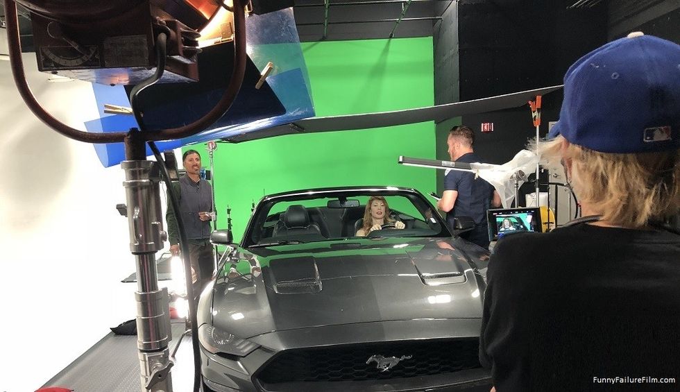 An actor driving in a Ford Mustage on a green screen.