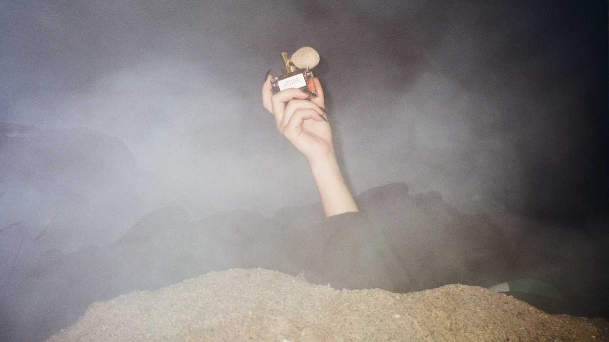 An arm emerging out of the ground with a perfum bottle