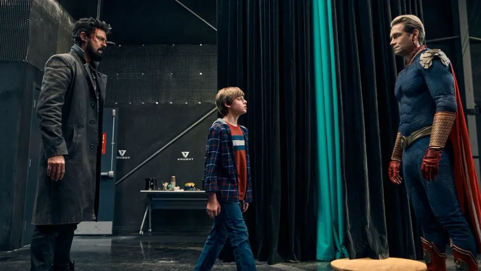 Billy Butcher, played by Karl Urban, and Homalander, played by Antony Starr, standing as a boy walks between them in 'The Boys'