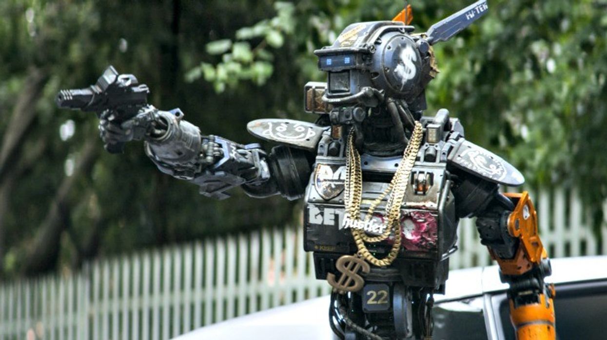 Chappie, a robot, wearing gold chains and pointing a gun in 'Chappie'