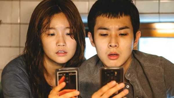 Choi Woo-shik as Kevin and Park So-dam as Jessica looking at their phones in Parasite