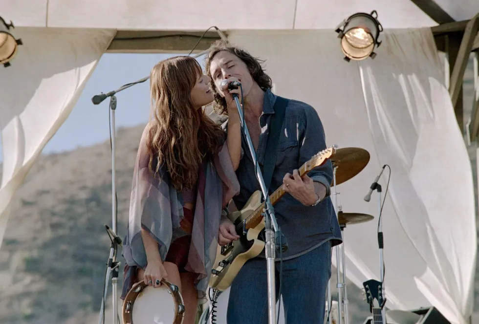 Daisy Jones, played by Riley Keough, and Billy Dunne, played by Sam Claflin, singing on stage in 'Daisy Jones & the Six'