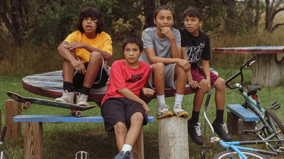 Four boys sitting at a bench in 'War Pony'