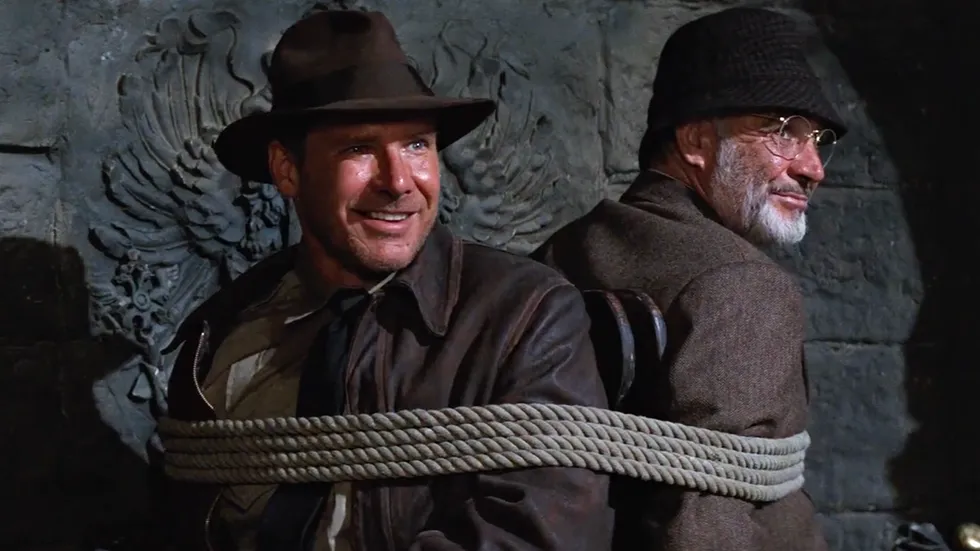 Harrison Ford and Sean Connery tied back-to-back to chairs in a classic scene from Indiana Jones and the Last Crusade