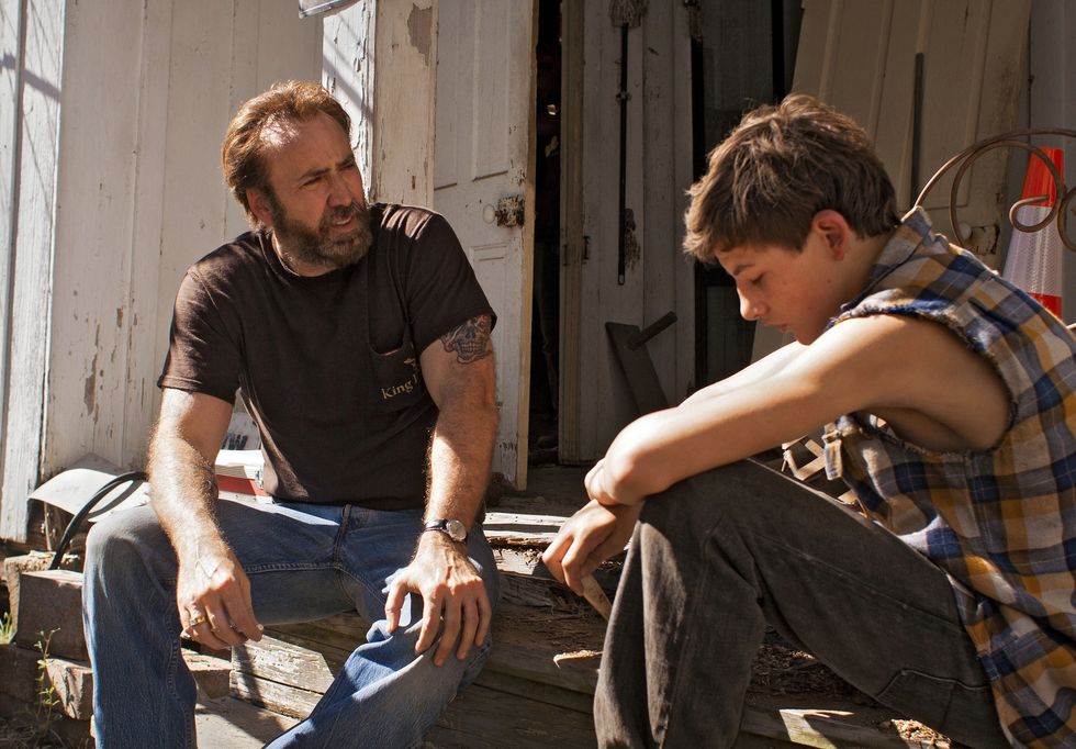 Joe Ransom, played by Nicolas Cage, and Gary Jones, played by Tye Sheridan, sitting by a barn in 'Joe'