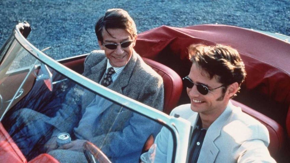 John Hurt as Giles and Jason Priestley as Ronnie sitting in a car and smiling in Love and Death on Long Island