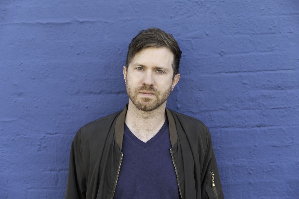 Matt Orenstein standing infront of a painted blue brick wall.