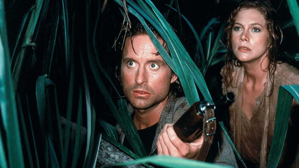 Michael Douglas peering through jungle leaves as Kathleen Turner looks on in Romancing the Stone