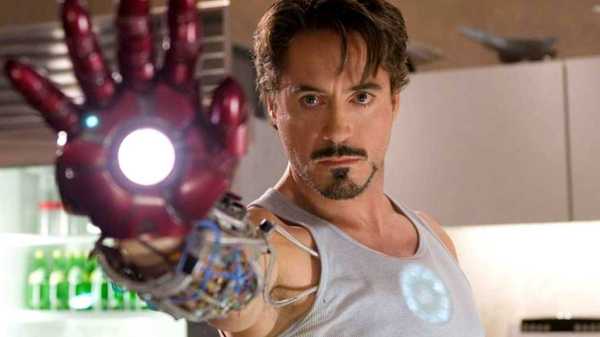 Robert Downey Jr as Tony Stark holding out a glowing metal hand in Iron Man 2008