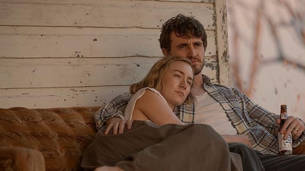 Saoirse Ronan as Henrietta and Paul Mescal as Junior snuggling on an outside couch in 'Foe'
