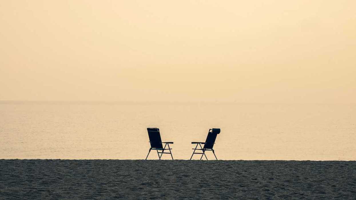 Two empty chairs are facing each other against the sea, symbolizin negative space.