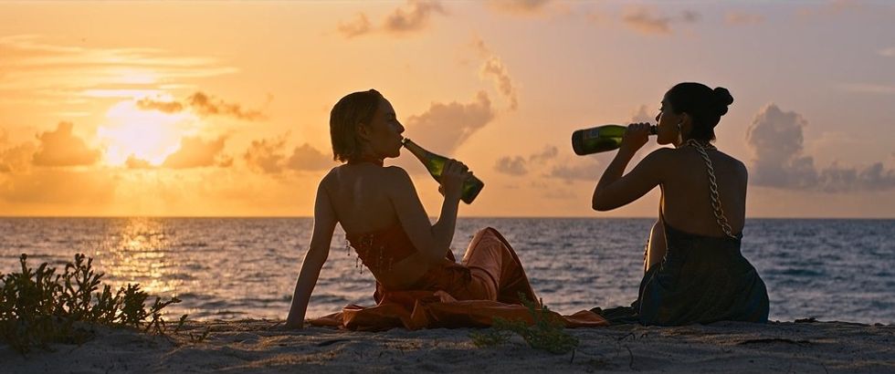 Two girls drinking champagne from the bottle on a beach in 'Do Revenge'