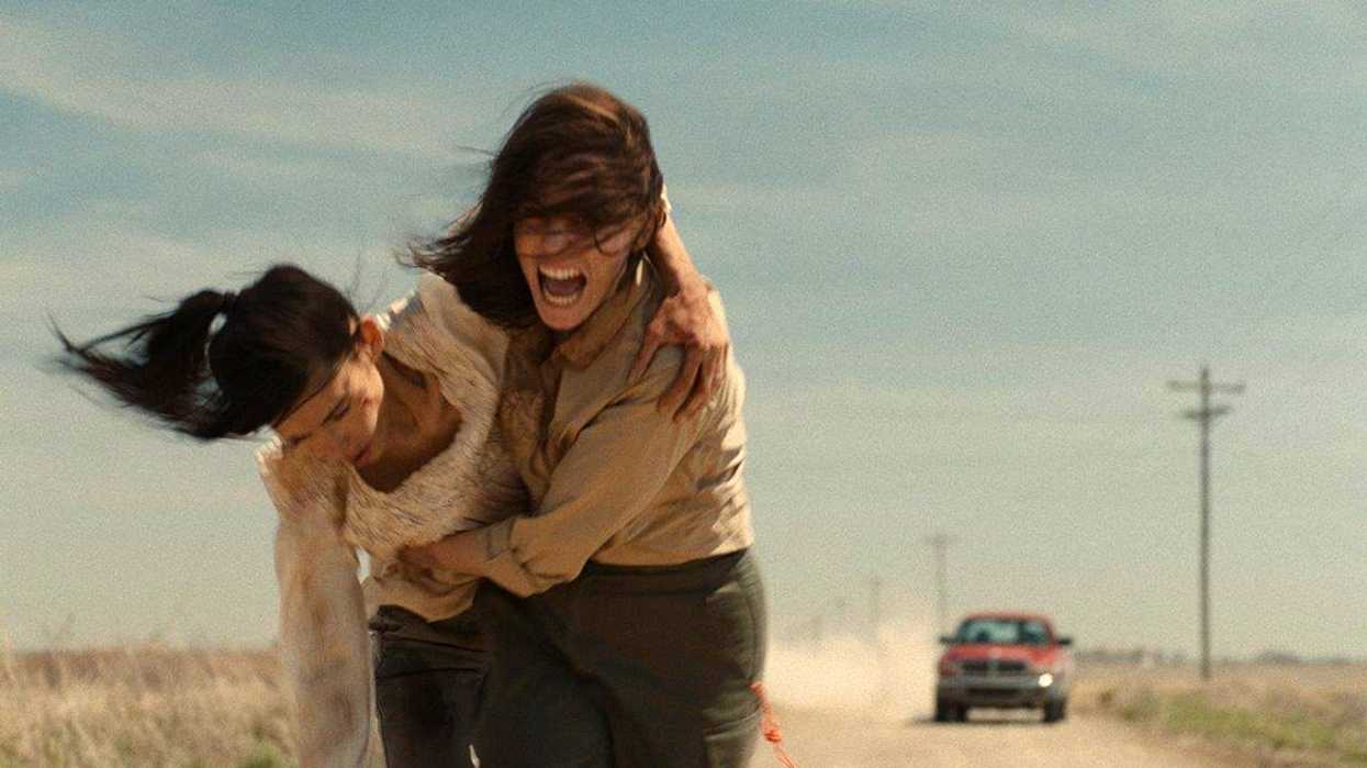 Two women running down a dusty road as a truck follows them in 'Herd'