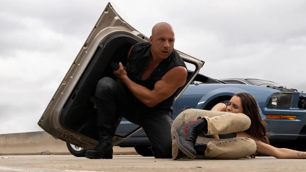 Vin Diesel as Dominic Toretto holding a car door for protection on the highway in 'Fast X'