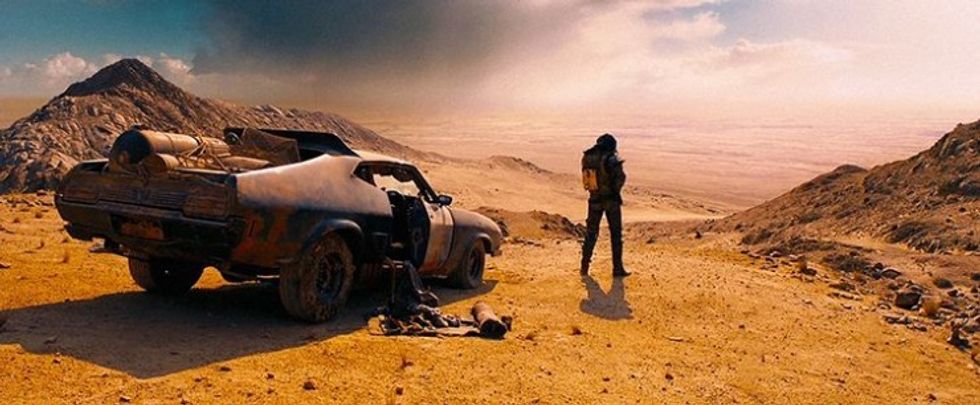 Wide shot of Max, played by Tom Hardy, standing in the desert next to his car in 'Mad Max: Fury Road'